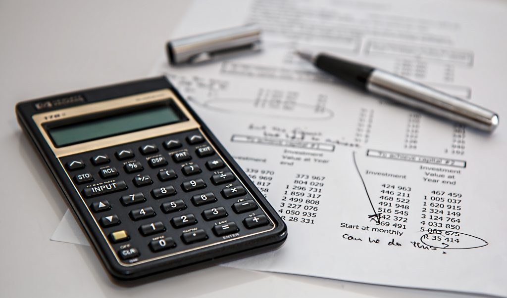 cost-effective maintenance - image of accounting items on a desk including calculator, pen, and paper financial report