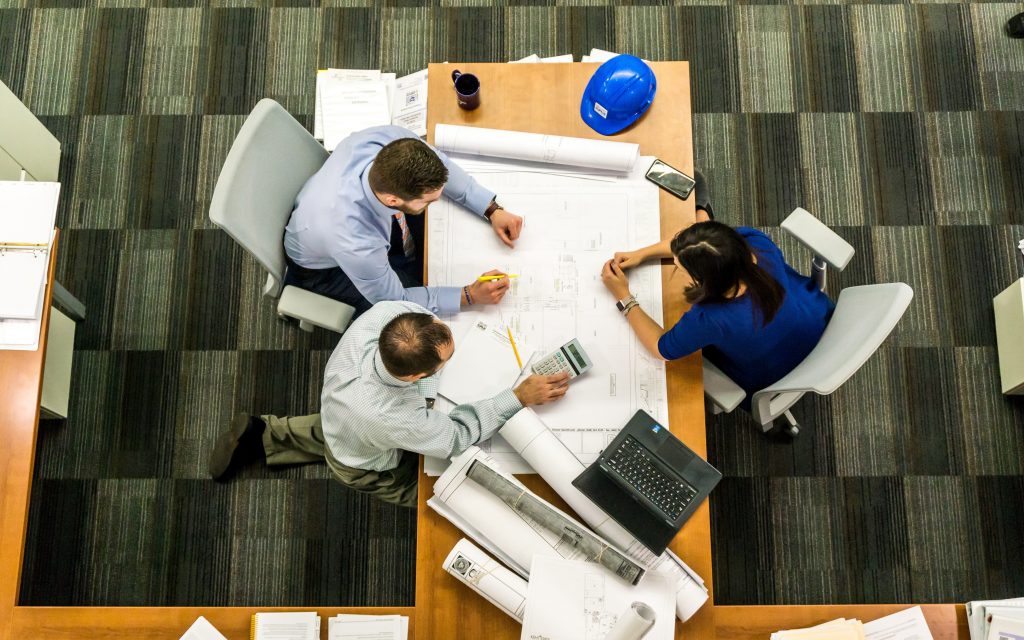 planned maintenance services - image shows overhead view of three people sitting around blueprints at a desk